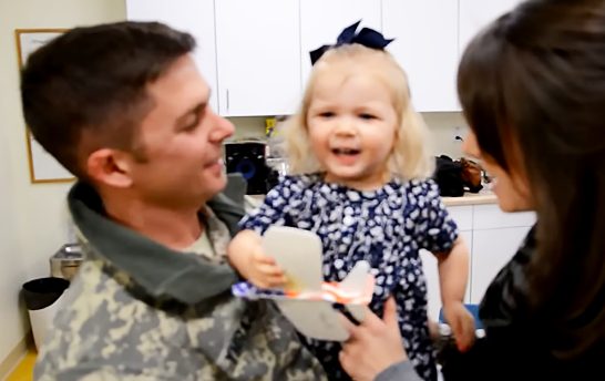Una niña de 2 años con mejillas sonrosadas está encantada cuando su papá soldado la sorprende.