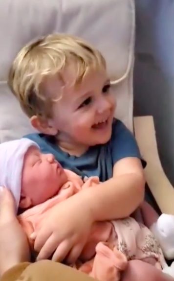 Niño pequeño sostiene a su nueva hermanita por primera vez, y es amor a primera vista.
