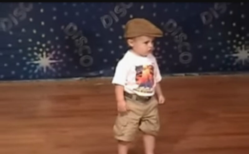 Un niño pequeño espera en el escenario para bailar: cuando comienza la música, el público se vuelve loco